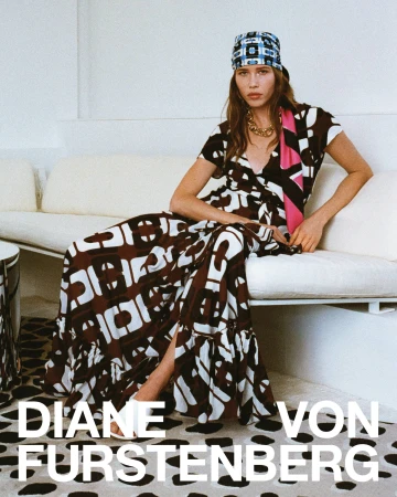 Model seated on a white sofa wearing a patterned wrap dress and printed headscarf for Diane von Furstenberg