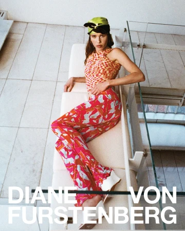 Model wearing a patterned top, pink trousers, and a lime headscarf reclining on white furniture in an architectural interior.