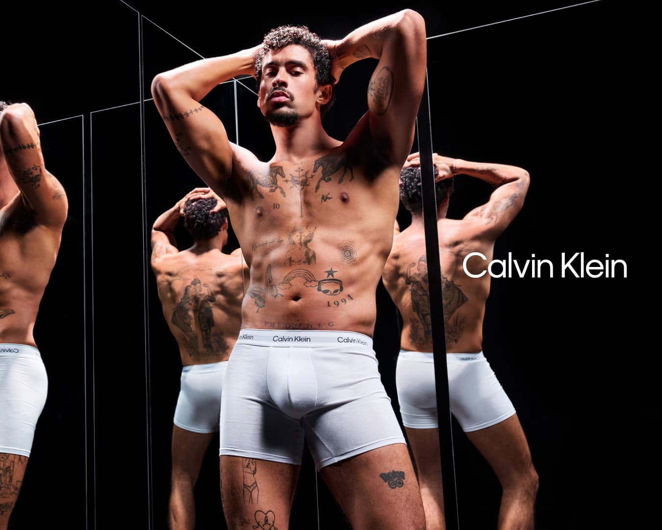 Bad Bunny wearing white Calvin Klein boxer briefs posing in front of multiple reflective mirrors against a dark background