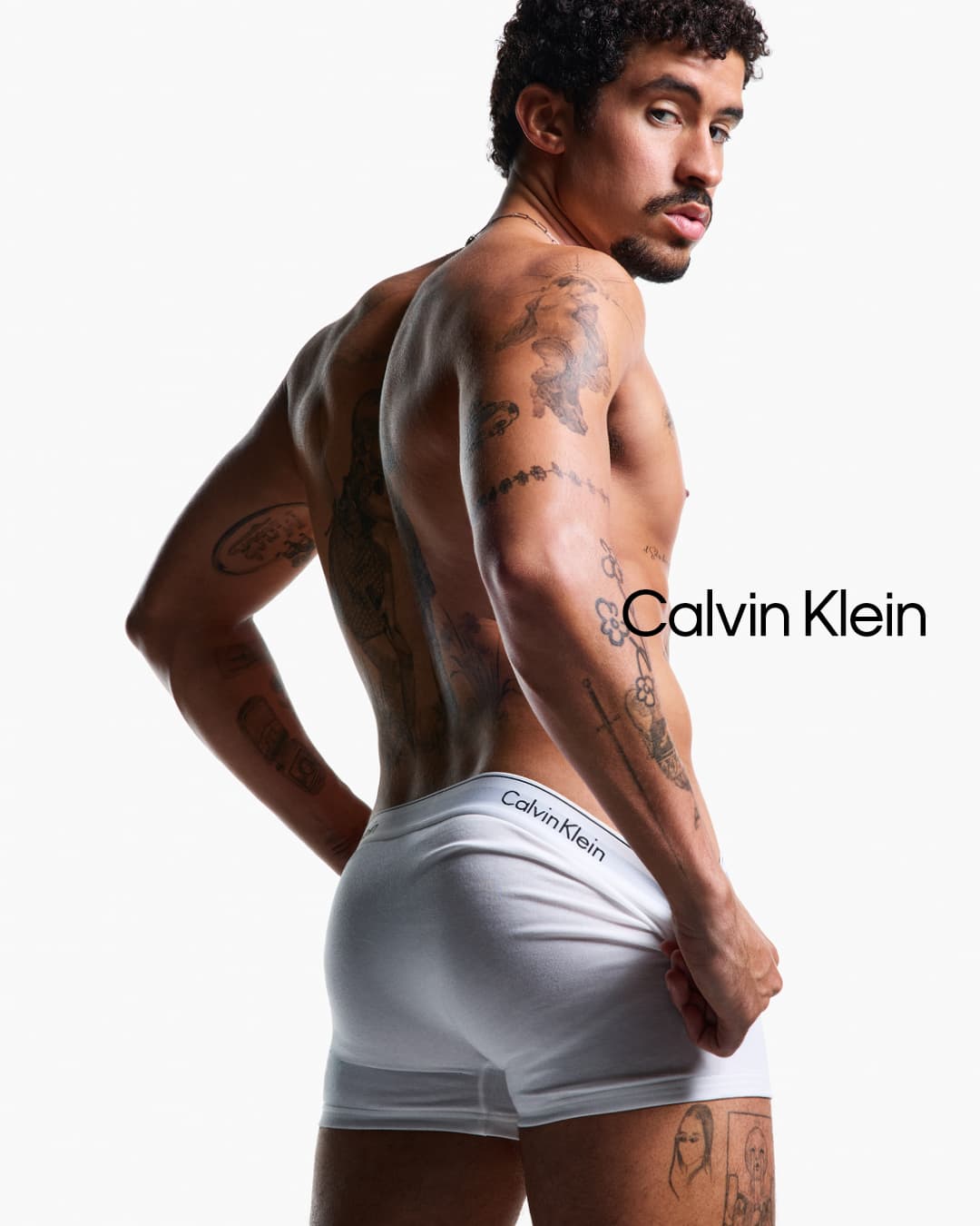 Bad Bunny wearing white Calvin Klein underwear in a studio portrait against a bright white background