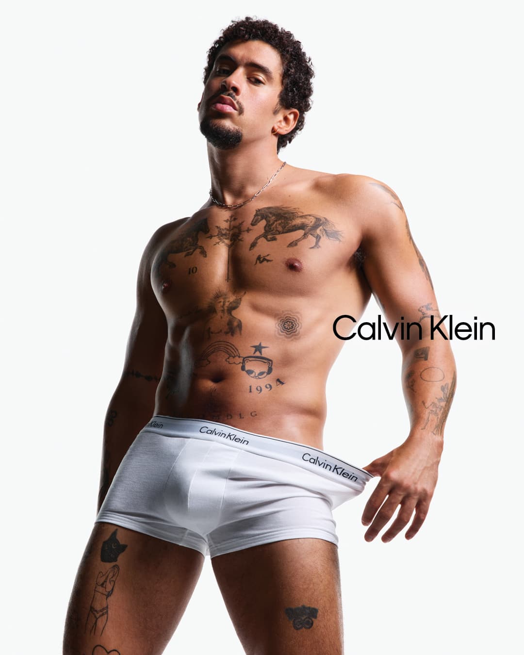 Bad Bunny posing shirtless in white boxer briefs against a plain white background for a Calvin Klein campaign