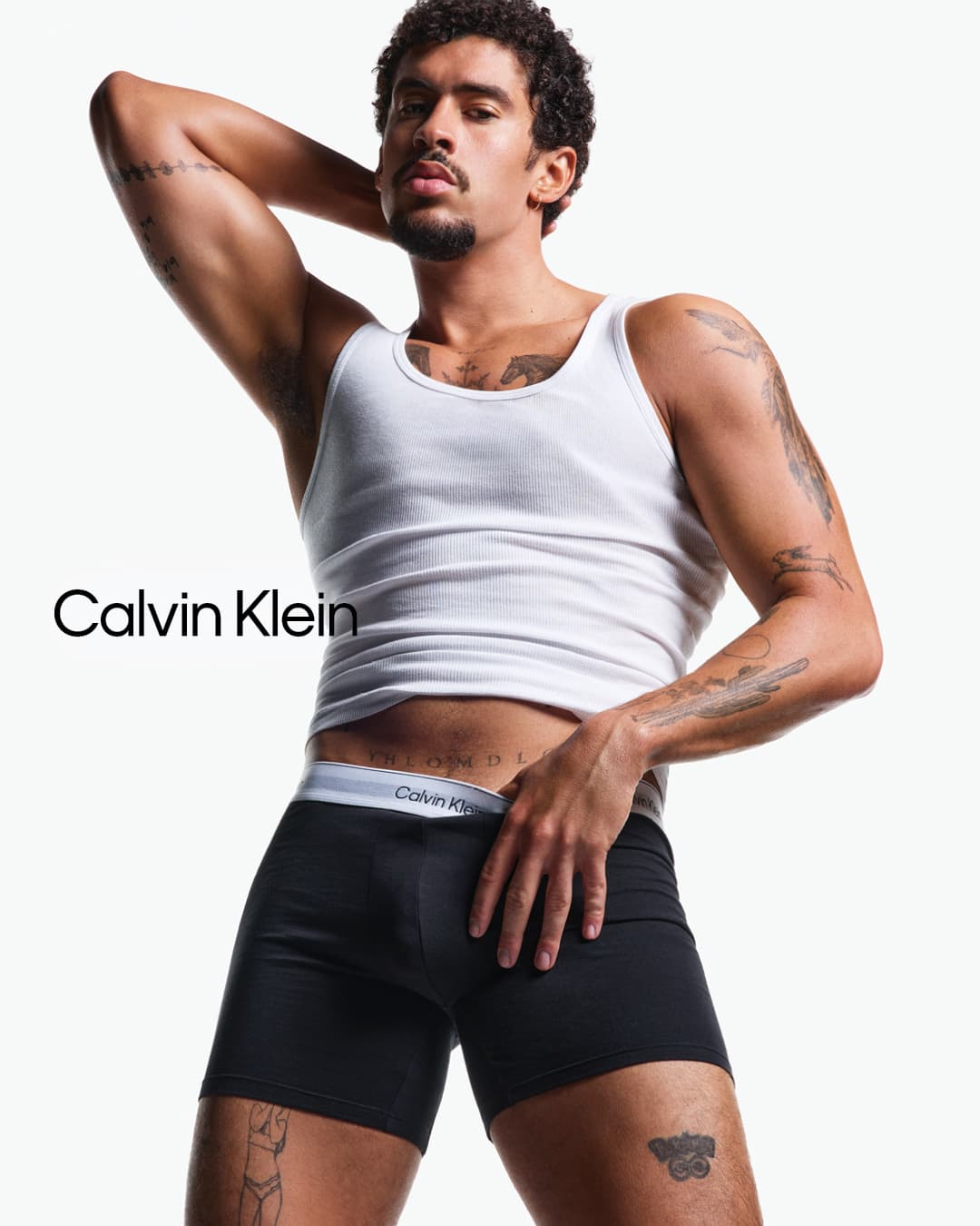 Bad Bunny wearing a white tank top and black briefs against a white background for Calvin Klein.