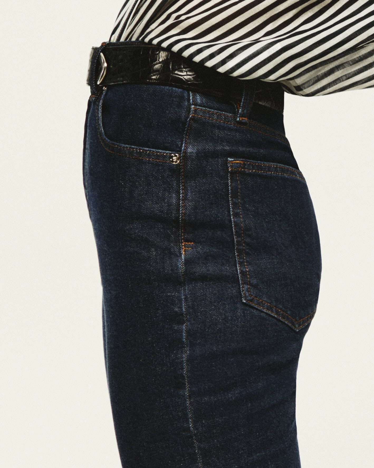 Close-up of dark denim jeans and a black leather belt worn with a black-and-white striped top