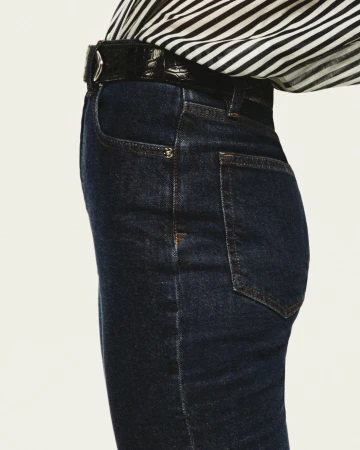Close-up of dark denim jeans and a black leather belt worn with a black-and-white striped top