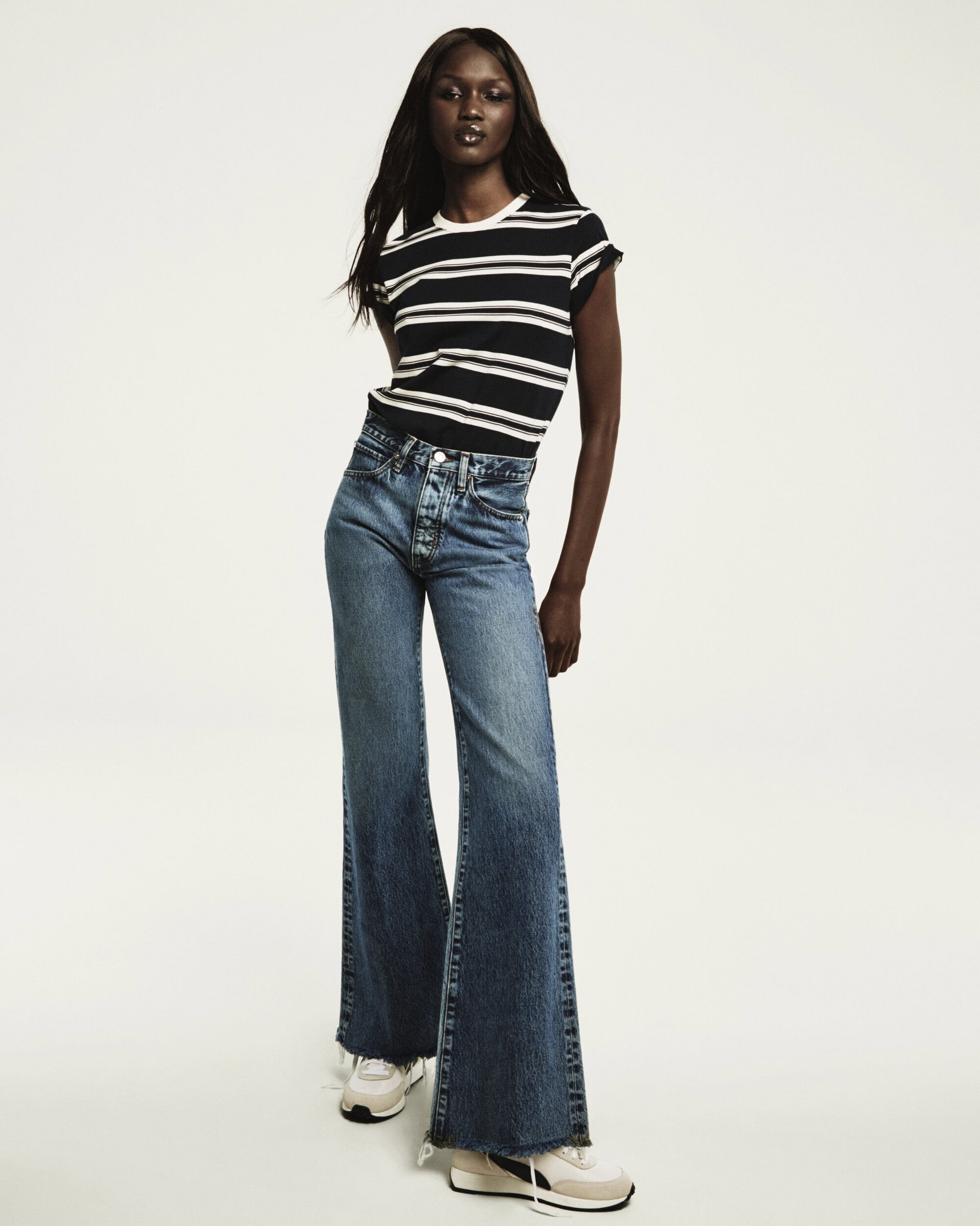 Model wearing a black and white striped t-shirt and denim jeans against a white seamless background for FRAME campaign.