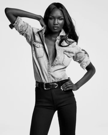 Abény Nhial wearing a denim shirt and dark trousers against a plain background for FRAME