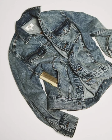 Acid wash denim jacket with a small comb tucked into the pocket against a neutral background for FRAME spring campaign