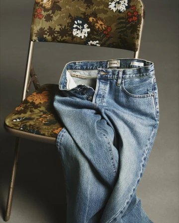 Blue denim jeans resting on a folding chair with floral patterned upholstery against a neutral dark background