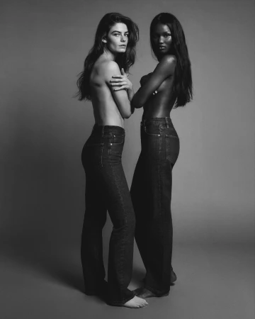 Two female models wearing dark denim jeans posing against a grey seamless studio background for FRAME Denim Spring 2025 campaign.