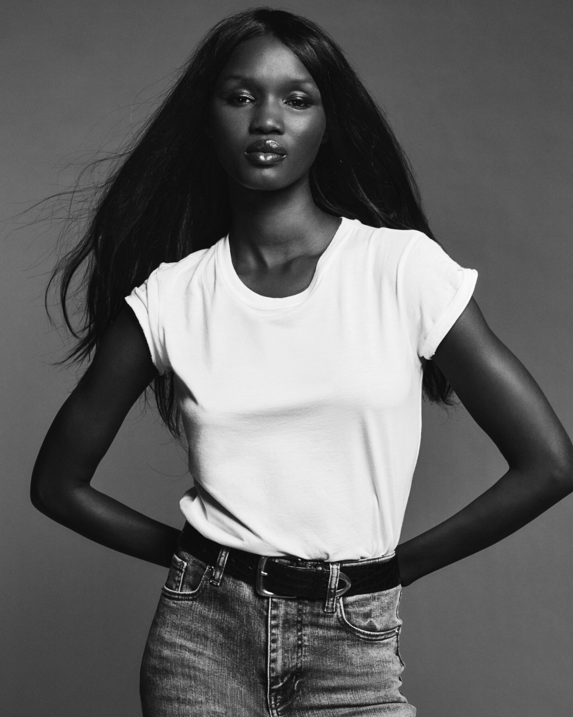 Model wearing a white t-shirt and denim jeans against a plain grey studio backdrop