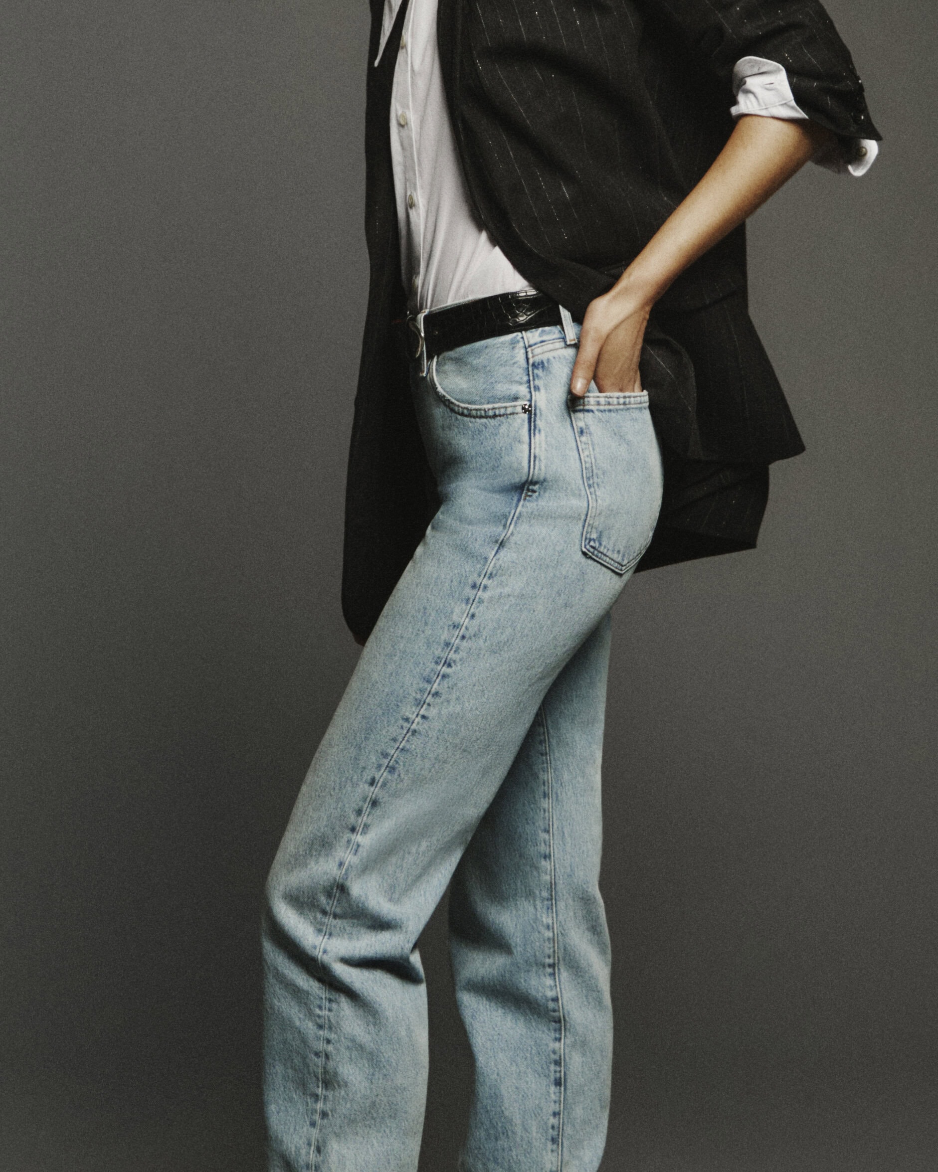 Model wearing light blue jeans, white shirt, and black blazer against a grey backdrop for FRAME Denim Spring 2025 campaign