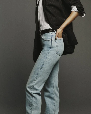 Model wearing light blue jeans, white shirt, and black blazer against a grey backdrop for FRAME Denim Spring 2025 campaign