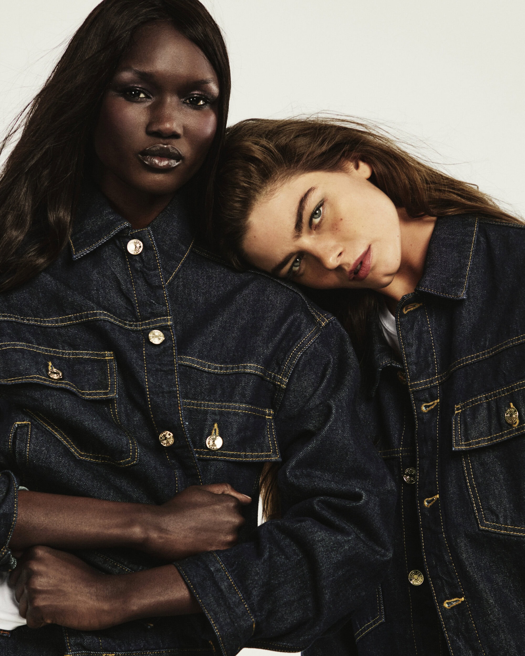 Two female models wearing dark denim shirts posing together against a plain white studio background.