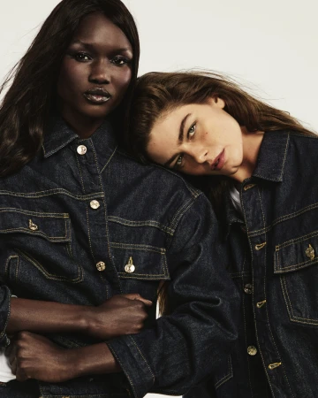 Two female models wearing dark denim shirts posing together against a plain white studio background.