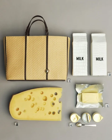 Flat lay ad campaign featuring a woven straw tote bag, two milk cartons, a large wedge of cheese, and butter.