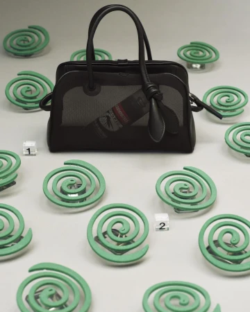 Black Jacquemus handbag surrounded by green mosquito coils on a grey studio background