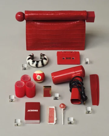 Red crocodile leather handbag arranged flat lay with red accessories including a hairdryer, cassette tape, comb, and numbered blocks.
