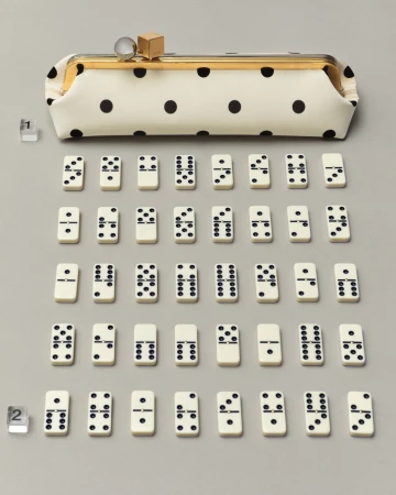 Polka dot pouch handbag with a gold clasp displayed above an arranged grid of dominoes on a grey seamless background.