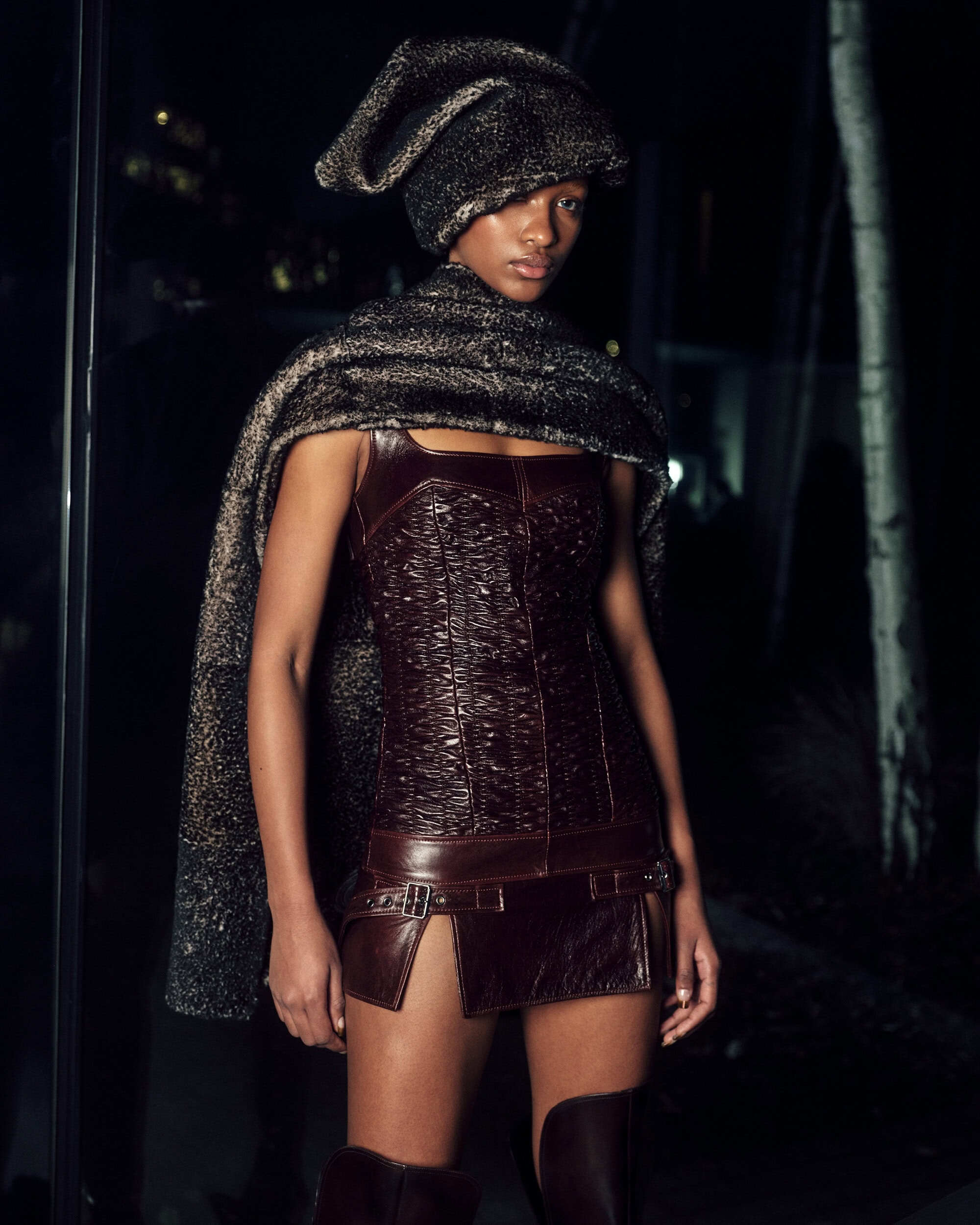 Model wearing a dark structured mini dress and a textured draped headpiece for KNWLS fall campaign.