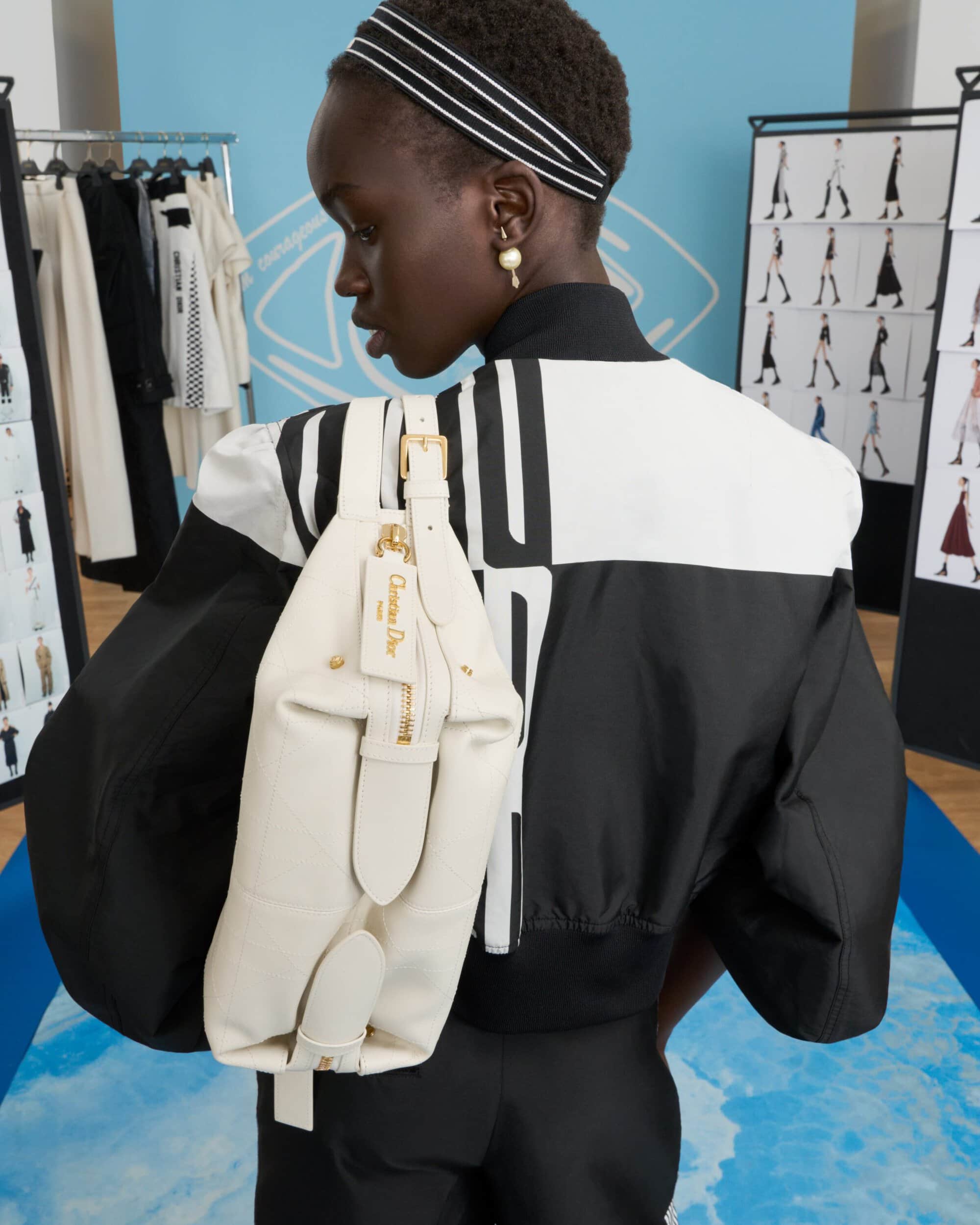 Model wearing a black and white jacket carrying a white leather bag in a studio setting