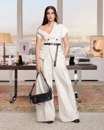 Sonam Kapoor wearing an off-shoulder white suit holding a black handbag in an elegant room interior