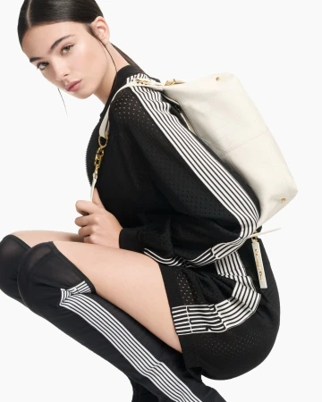 Model crouching against a white background wearing a black athletic dress and carrying a white backpack