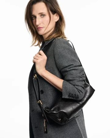 Camille Cottin wearing a grey coat and holding a black leather shoulder bag against a white background