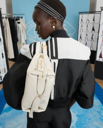 Model wearing a black and white jacket carrying a white leather bag in a studio setting
