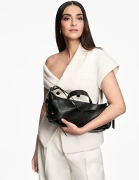 Woman in white asymmetric blazer holding a black leather handbag against a plain white background