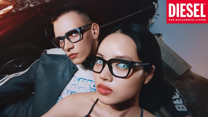 Two models wearing thick black-rimmed glasses and dark jackets in a dimly lit setting for Diesel Spring 2025 campaign.