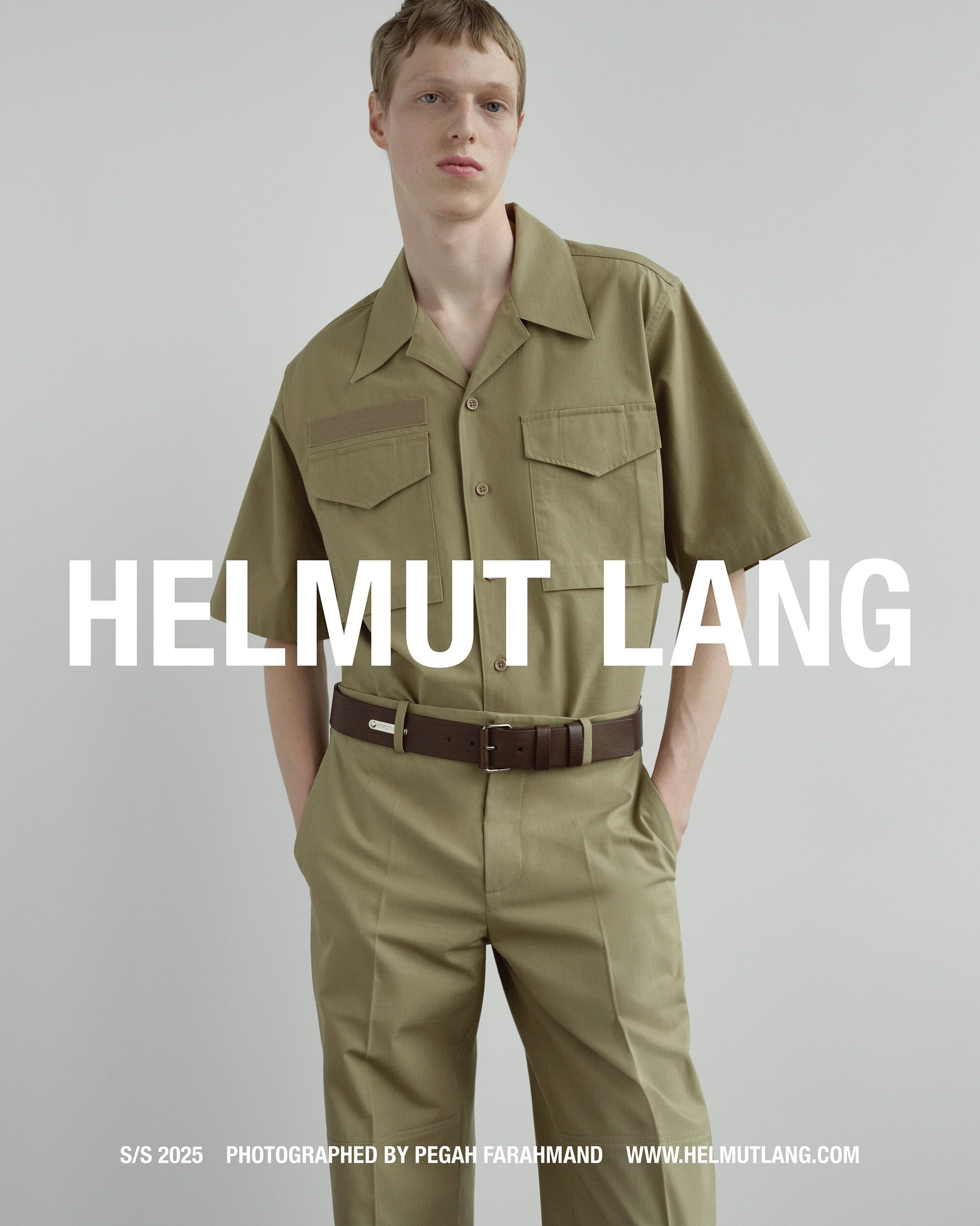 A male model wearing an olive green short-sleeve utility shirt and matching trousers against a plain grey background