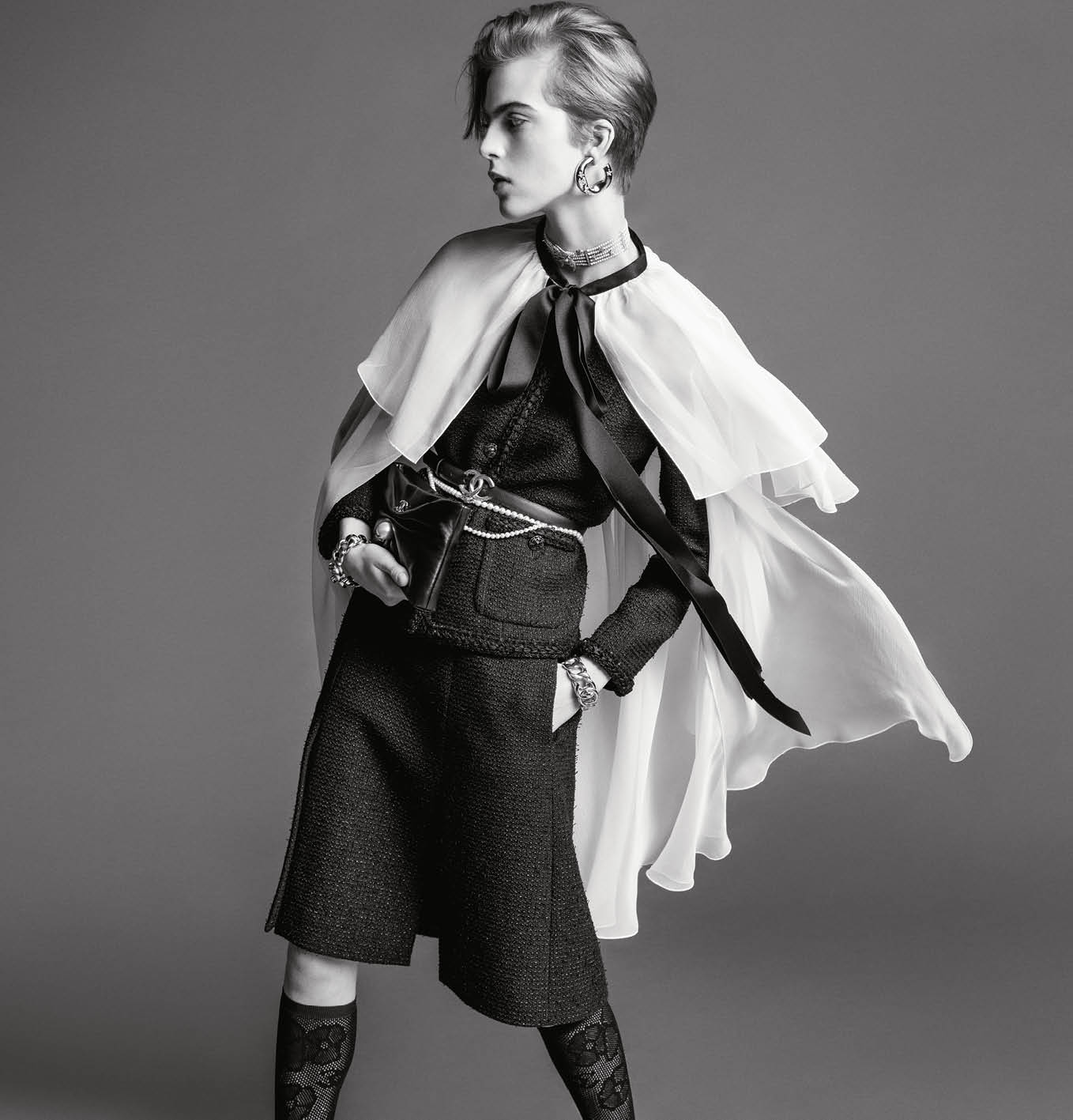 Model in tweed jacket and cape wearing jewellery against grey backdrop for Chanel spring 2025 ad campaign