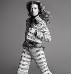 Model wearing a tweed suit and holding a quilted handbag against a seamless grey backdrop for the Chanel Spring 2025 ad campaign.