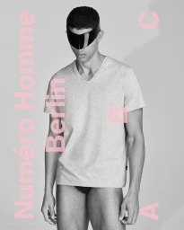 Model wearing a black visor and grey v-neck t-shirt against a grey background with pink typography