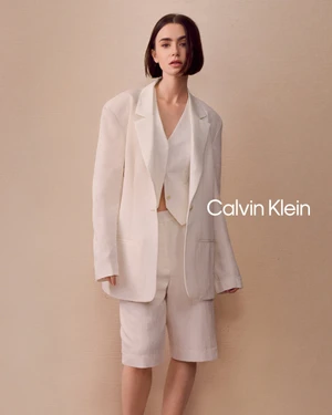 Lily Collins in a white blazer and matching shorts against a textured neutral background for Calvin Klein.