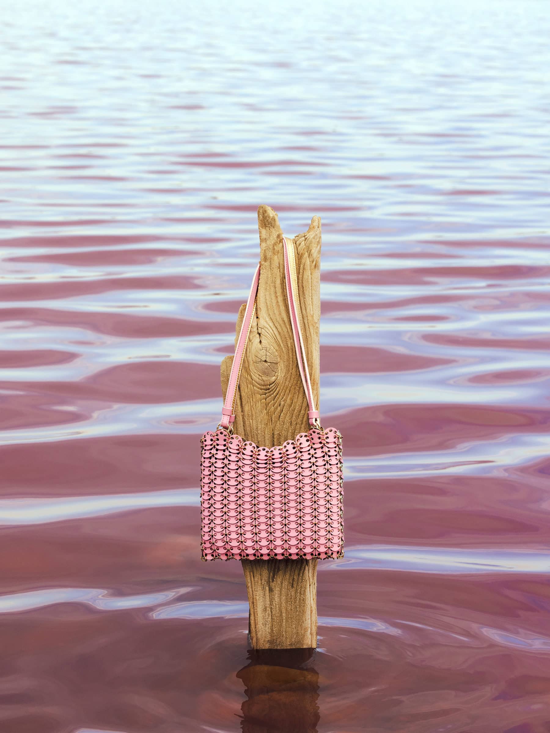 Pink chainmail handbag hanging from a weathered wooden post standing in calm pink water
