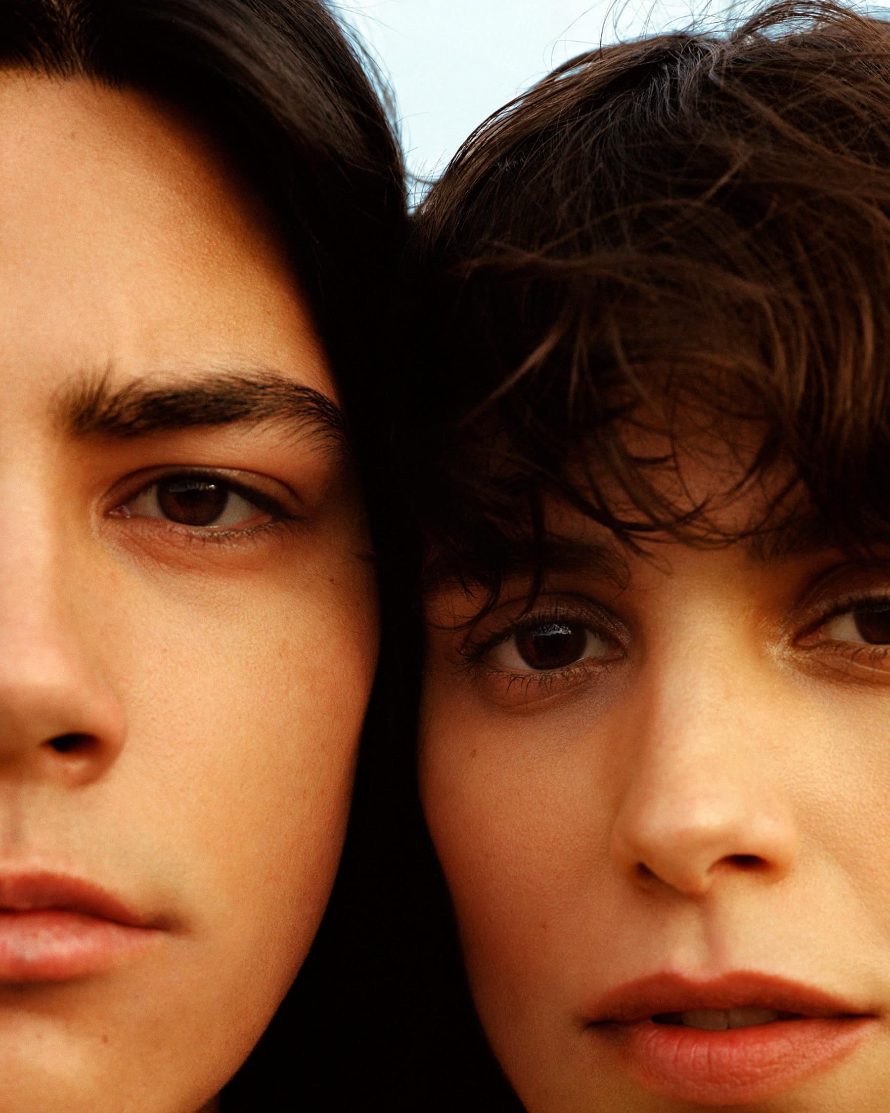 Close-up portrait of two models side by side with dark hair against an outdoor sky background for Rabanne Spring 2025 campaign.