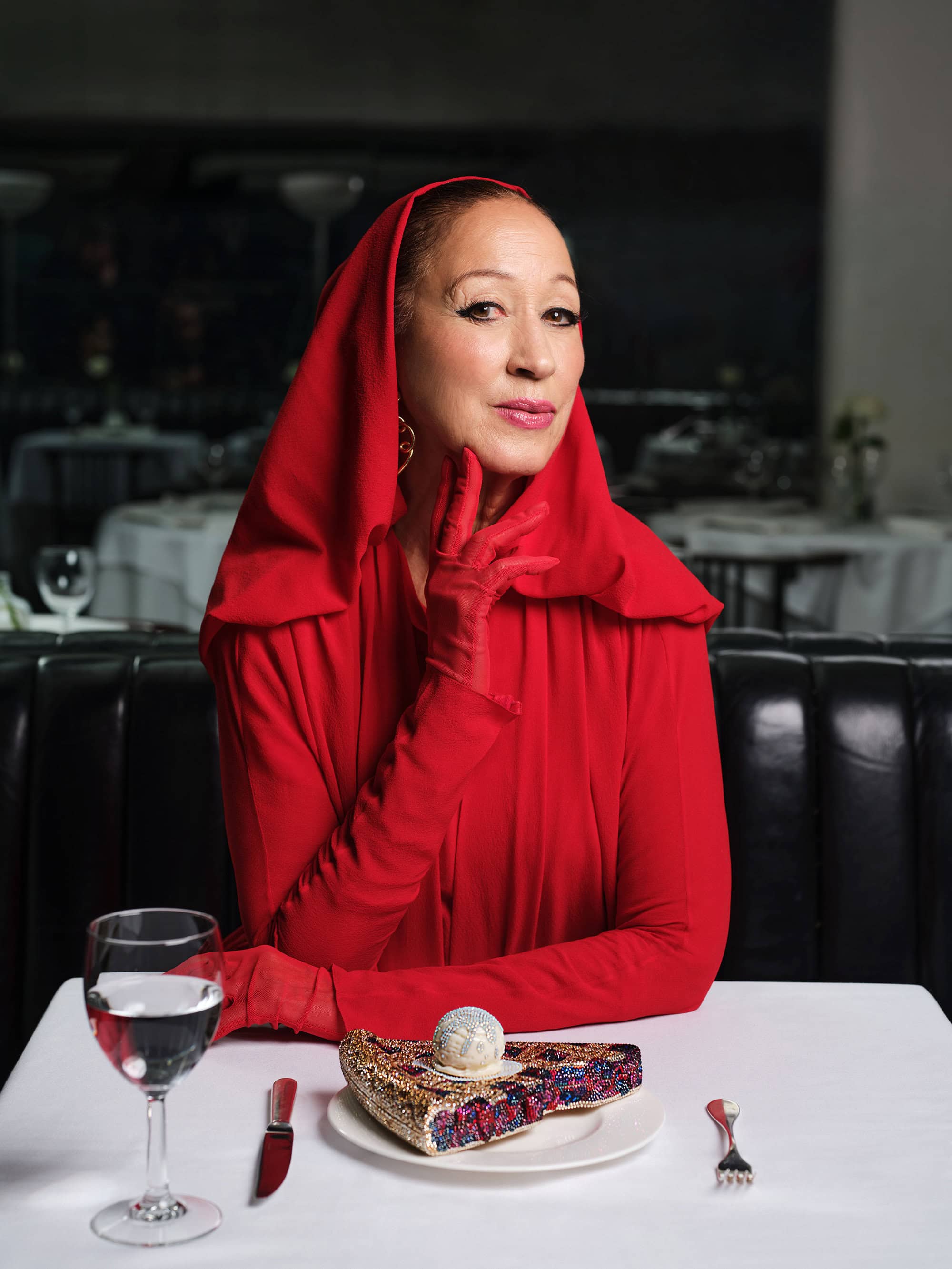 Elderly woman wearing red hooded dress and gloves at restaurant table with dessert