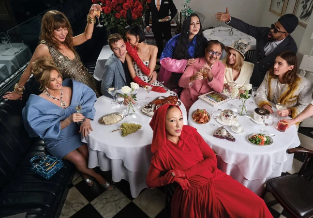 Group of diverse fashion figures gathered around dining tables in a high-end restaurant setting for Neiman Marcus.