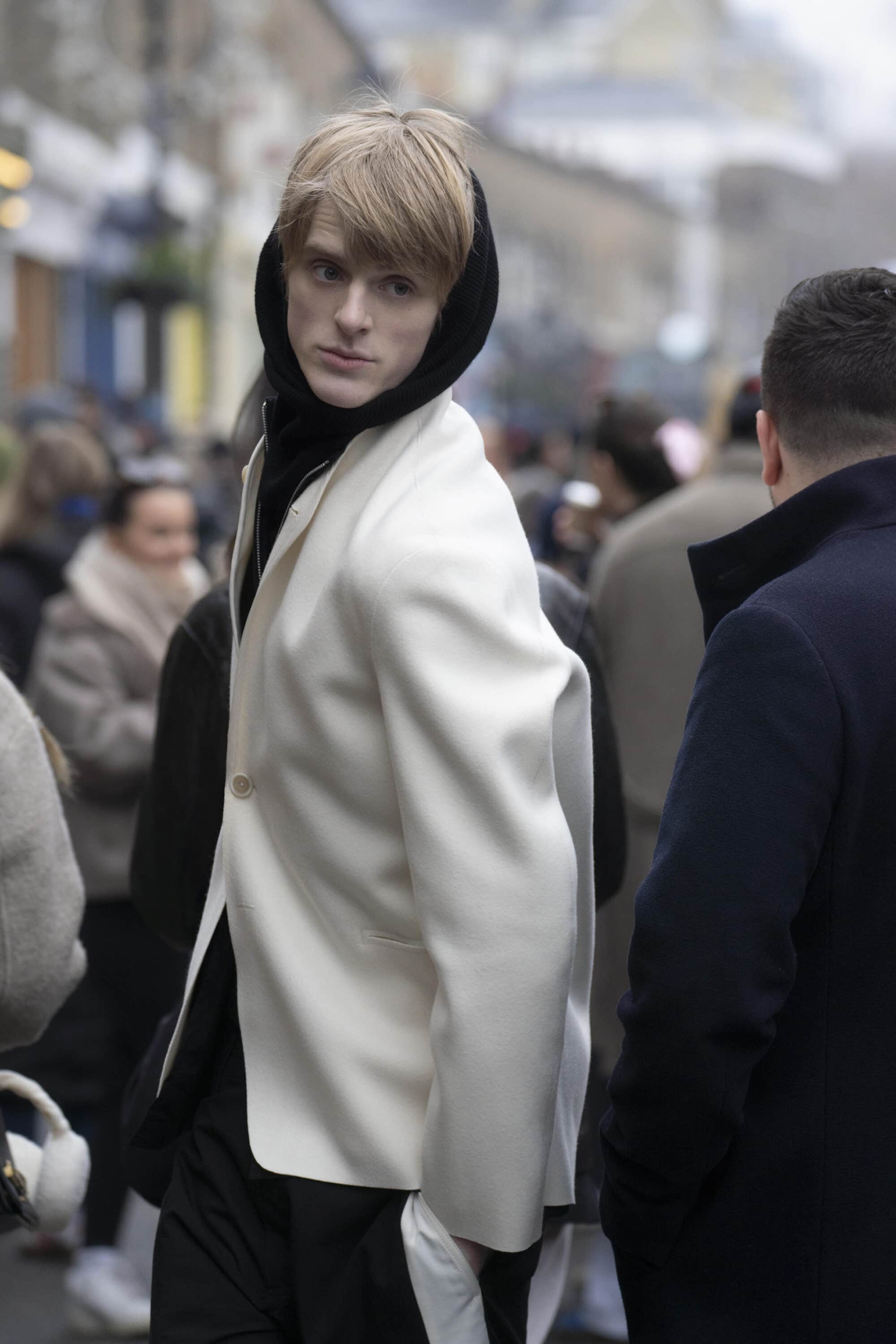 Blonde male model wearing a white blazer and black hoodie on a busy city street for Derrick Intermission campaign
