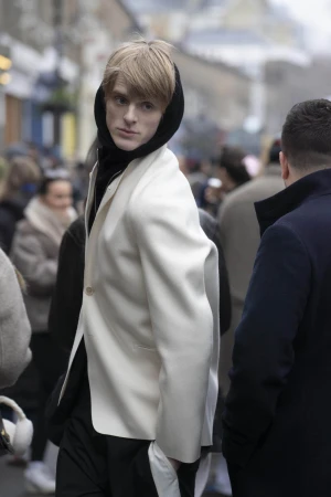 Blonde male model wearing a white blazer and black hoodie on a busy city street for Derrick Intermission campaign