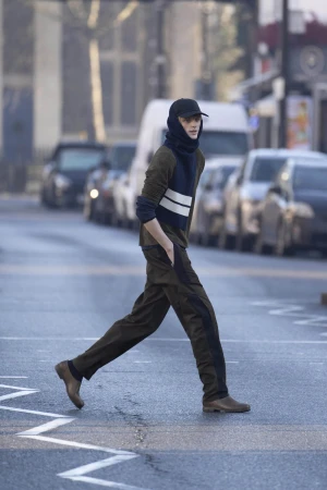Model wearing dark trousers and baseball cap walking across a city street for the Derrick Intermission campaign