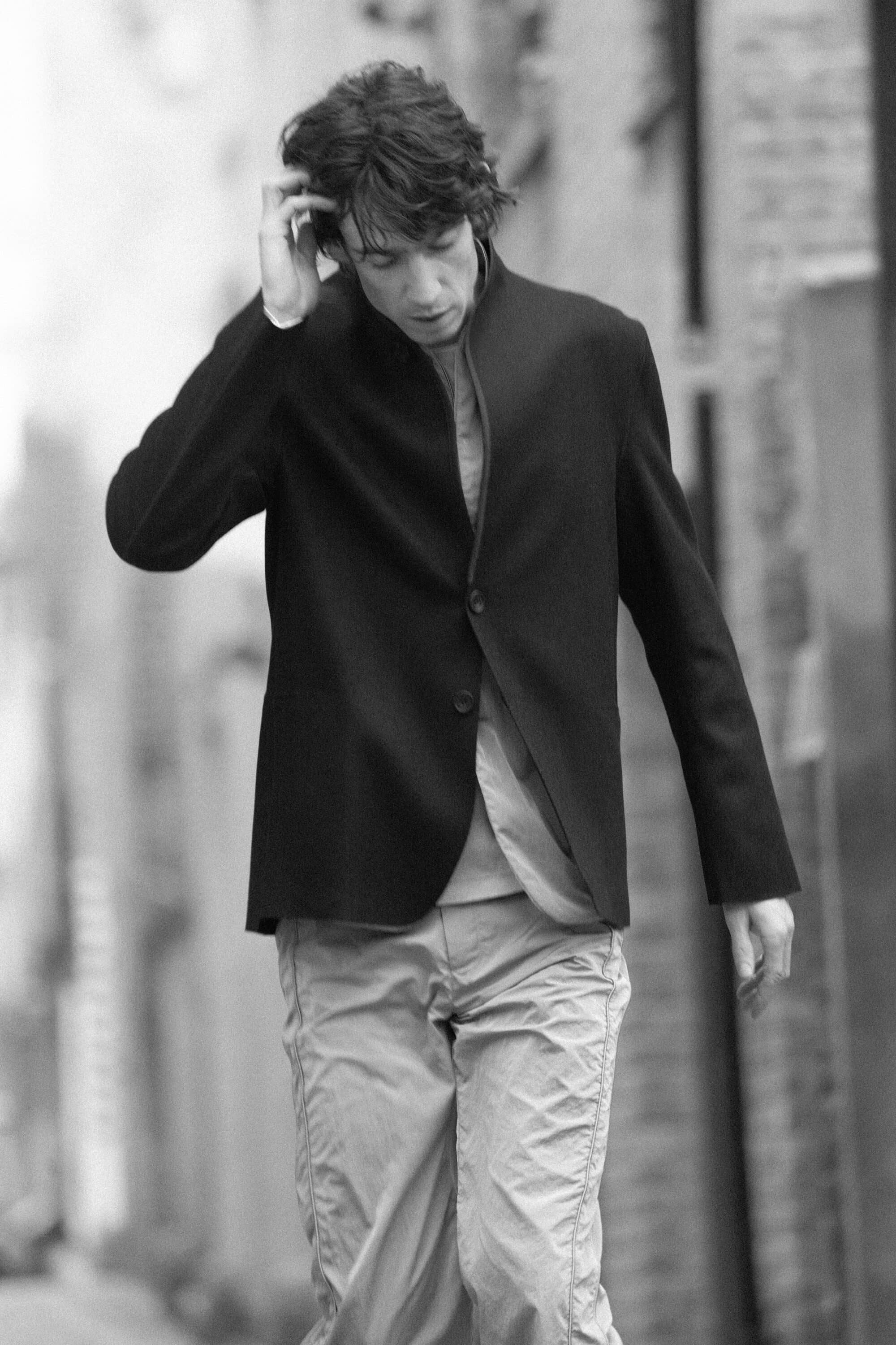 Monochrome portrait of a man in a dark jacket touching his hair outdoors