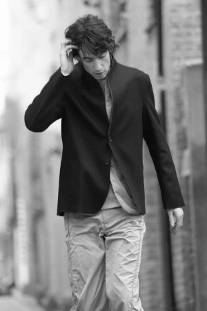 Monochrome portrait of a man in a dark jacket touching his hair outdoors