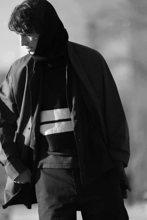 Man wearing a dark hooded sweater and jacket against an out of focus background