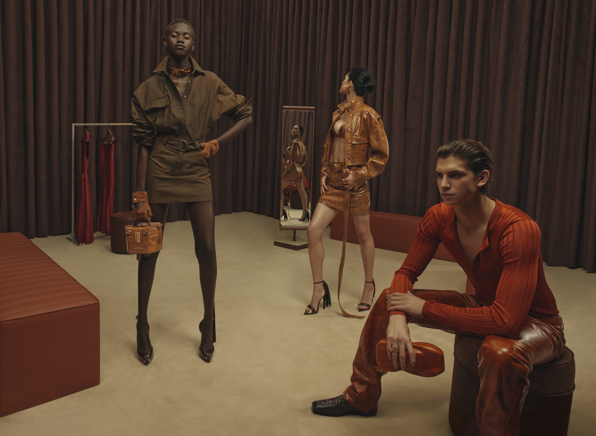 Three models posing in a studio set with brown drapes showcasing a Ferrari fashion campaign styled by Jacob K.