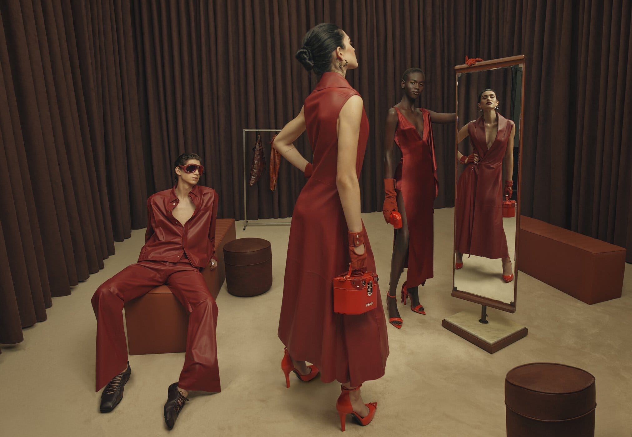 Models in red leather clothing posing in a studio set with brown curtains and matching red accessories.