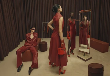 Models in red leather clothing posing in a studio set with brown curtains and matching red accessories.
