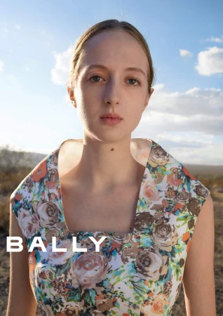 Model wearing a floral print dress outdoors against a desert landscape under a clear sky for Bally spring 2025 campaign