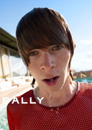 Close-up portrait of a young man with wet hair wearing a red mesh shirt outdoors near a pool for the Bally Spring 2025 ad campaign.